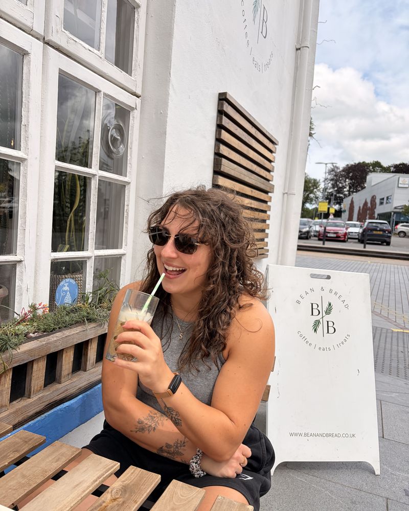Hannah outside a café in sunglasses, with an iced coffee